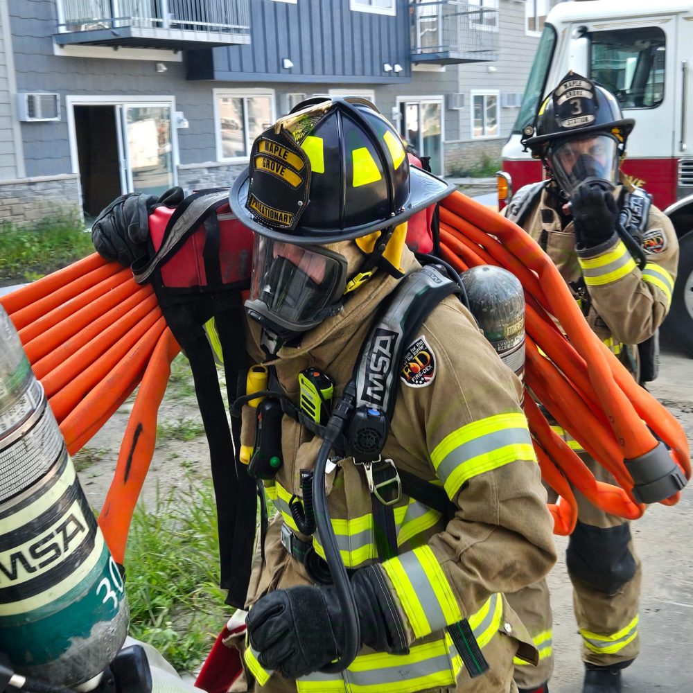 A Maple Grove firefighter in full turnout gear carrying firehouse on their should.